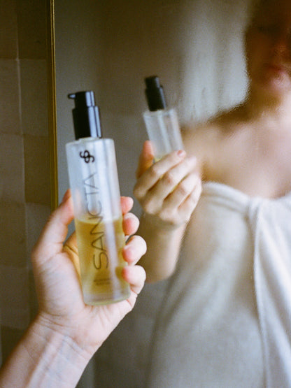 Sancta Solis Nourishing Body Oil skincare product held in front of a mirror.
