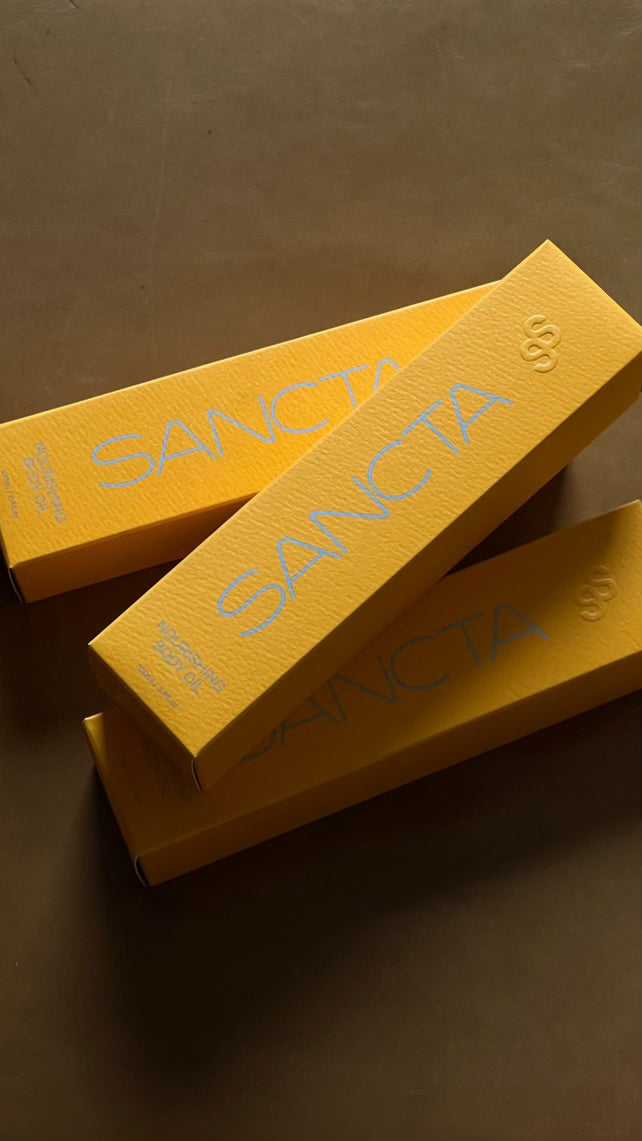 Sancta Solis Nourishing Body Oil Secondary Box Packaging. Blind emboss logo on yellow box with a blue logo.