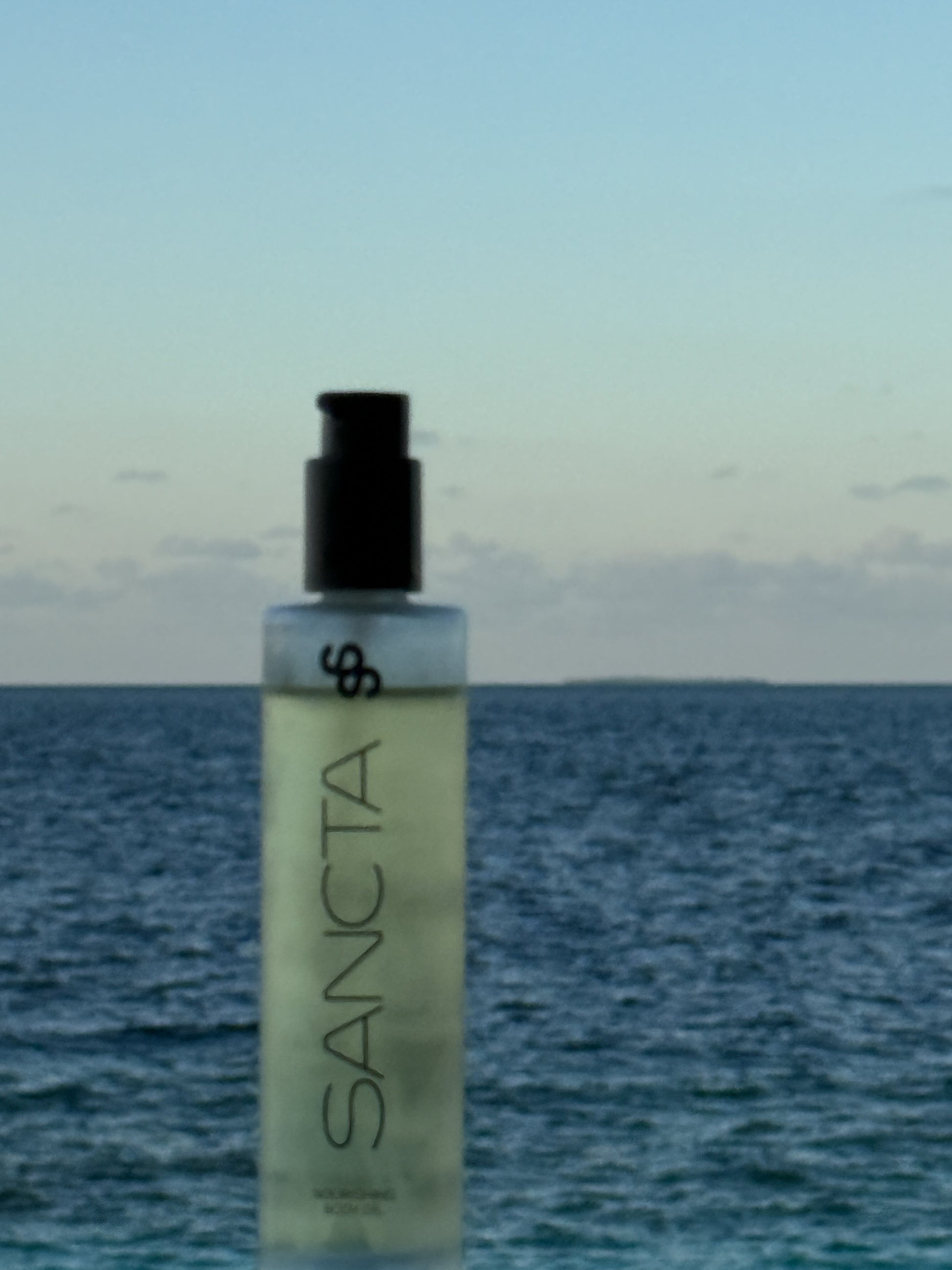 Bottle of Sancta Nourishing Body Oil with ocean in the background